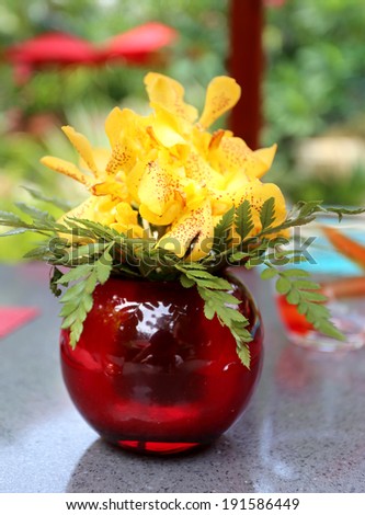 bright yellow bouquet of orchids in a red glass vase on the table