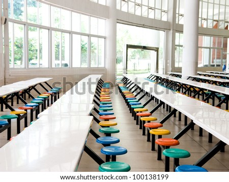 Clean school cafeteria with many empty seats and tables.