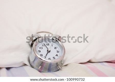 Old fashioned alarm clock with bed in the morning.
