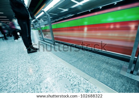 People waiting in subway station with motion blurred train beside.