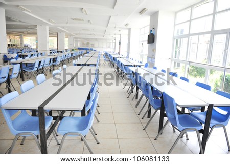 Clean school cafeteria with many empty seats and tables.
