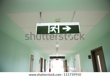 exit sign suspended from the ceiling of hospital corridor exit sign suspended from the ceiling of hospital corridor