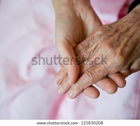 Young girl's hand touches and holds an old woman's wrinkled hands.