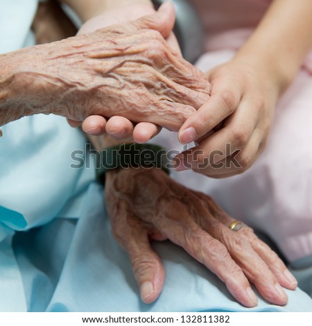 Young girl\'s hand touches and holds an old woman\'s wrinkled hands.