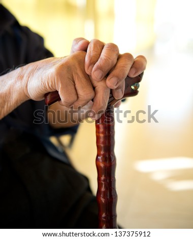 Old man sitting with his hands on a wooden walking stick.