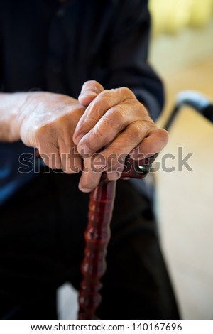 Old man sitting with his hands on a wooden walking stick.