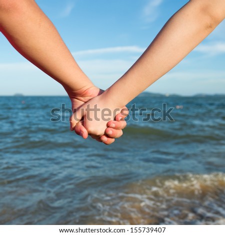 Summer couple holding hands in front of the sea.