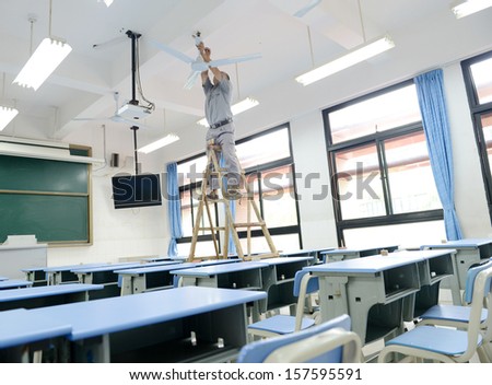 People repairing the fan in a empty classroom.