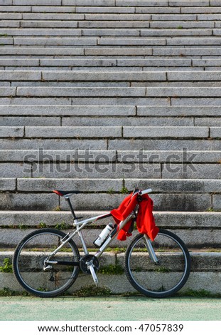 A bicycle leaning against the stone stairs, with a red clothes on it.