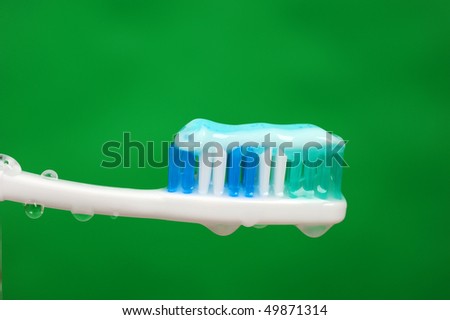 A wet toothbrush with some toothpaste on it, and drops of water over green background.