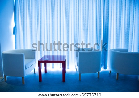 Office cafe bar with comfortable chairs and red table beside curtain.