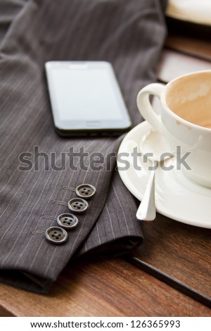 Cup of coffee on table with suit jacket and cell phone in sun concept out of office taking a break mobile office