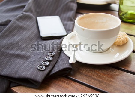 Cup of coffee on table with suit jacket and cell phone in sun concept out of office taking a break mobile office