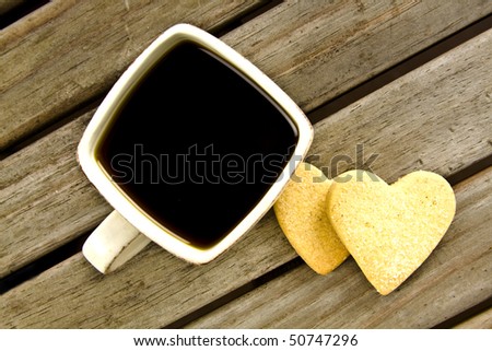 Coffee cup with black strong coffee on old wooden table with short bread heart biscuits covered in sugar.