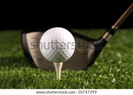 Close up white golf ball on white tee secured in green grass(artificial turf) with 1 wood driver (golf club) behind the ball ready to be hit, black background, space for copy to be added.