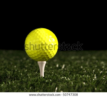 Close up of bright yellow golf ball on white tee in the ground, (artificial turf) green grass fading into a black backround(for copy), shallow depth of field with focus point on the front of the ball