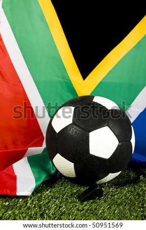 Soccer ball on green grass(artificial turf) with a referee whistle and south african flag as background
