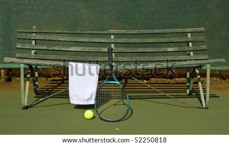 Tennis court with bench, white towel, racket and ball on sunny day