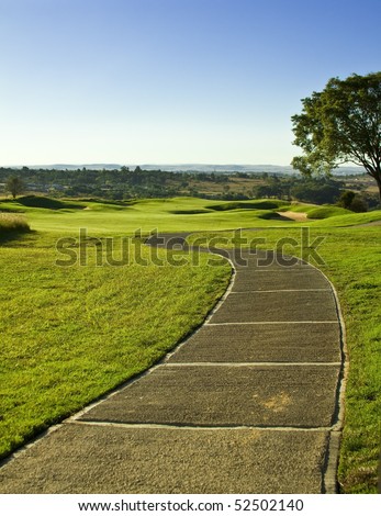 Golf course path leading the way to the fairway with bunkers (sand traps) hills and trees in late afternoon sun