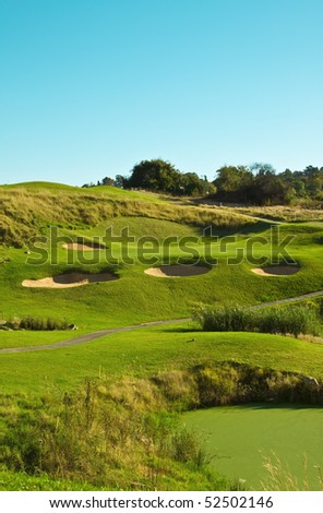 Golf course hole ,par 3 with bunkers and path running next to it on a sunny afternoon
