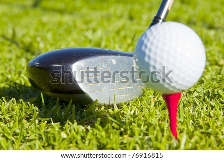 white golf ball on red tee in grass with driver close up ,ready to be hit