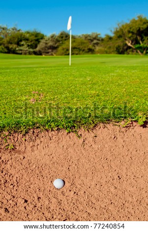 golf ball in a big bunker with trail of ball hitting sand green and flag infront