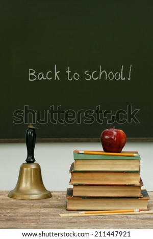 School bell and books on desk with chalkboard in background