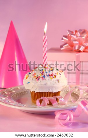 Small cupcake with candle, gift and pink party hat