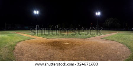 Panorama night photo of an empty baseball field at night with the lights on taken behind home plate and looking out across the pitcher\'s mound onto the field.