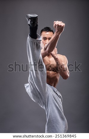 Young asian man workout over grey background karate kick
