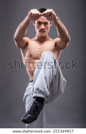 Young asian man workout over grey background karate kick