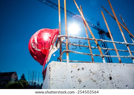 Worn Red Hard Hat reinforced concrete steel with big crane and sun in background on a construction site