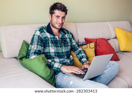Handsome young man sitting on couch working on his laptop