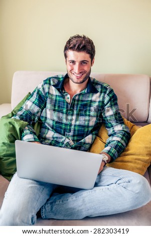 Handsome young man sitting on couch working on his laptop