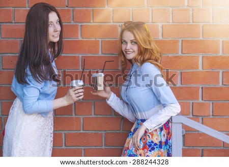 Two girls with cups of coffee talk on the background wall