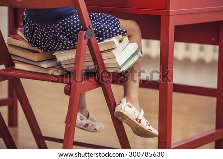 Little girl sitting on the chair and on the books at school in class. Body parts, training, education, preschool, will grow.