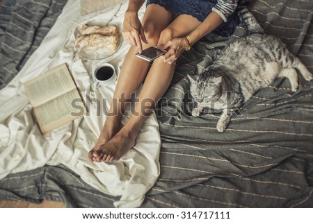 Beautiful woman model with coffee, pastries, home phone on the blanket with a cat