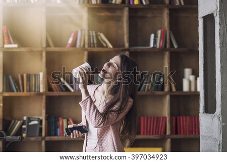 Smart beautiful young woman in headphones with a glass of coffee in his hand instead of a microphone dancing and singing to the music