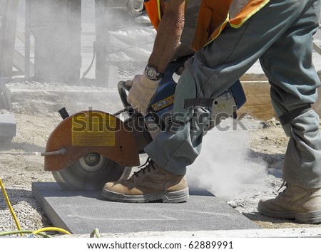Stone cutter at work on construction site, creating a cloud of dust