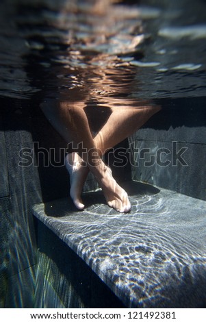 Crossed legged feet in pool with water ripple reflection on step