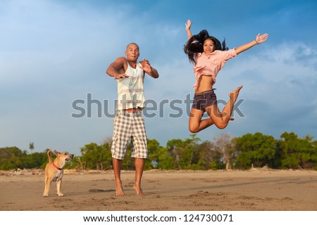 young couple jumping in the air on the beach with their dog
