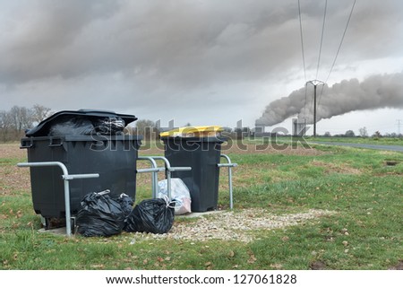 Household waste container in front of nuclear power plant with dark smoke