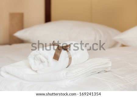 White towels with brown ribbon folded on white sheets in a bedroom