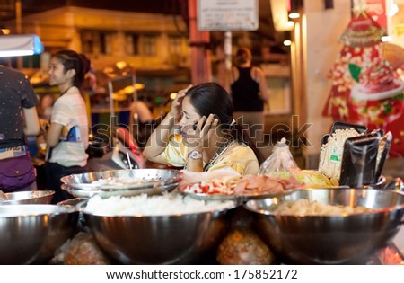 BANGKOK, THAILAND - JANUARY 9, 2012: Vendor on a street food stall talks on the phone on Khao San Road. Everyday thousands of tourists and locals buys food on these stalls.
