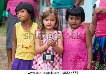 ELLA, SRI LANKA - MARCH 2, 2014: Little blonde girl posing with two local girls. Ella is famous for the tea plantations and stunning views across the countryside.