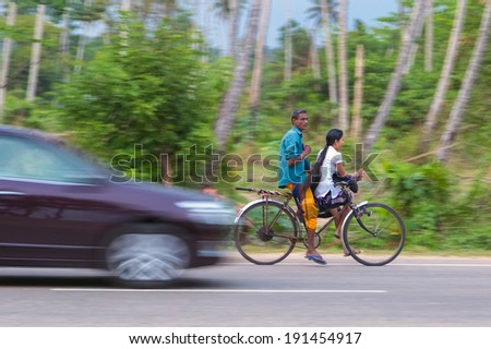 WELIGAMA, SRI LANKA - MARCH 7, 2014: Couple riding a bicycle on local road. Tourism and fishing are two main business in this town.