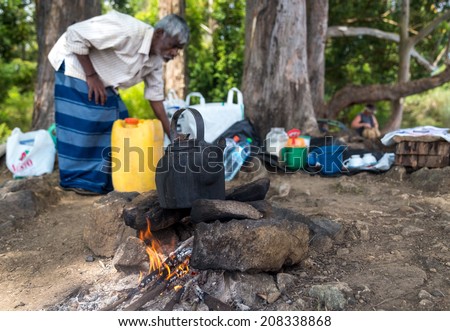ELLA, SRI LANKA - MARCH 2, 2014: Elderly local man boiling water in a pot on camp fire in forest.