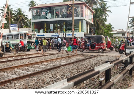 HIKKADUWA, SRI LANKA - FEBRUARY 22, 2014: Pedestrians and vehicles on rail crossing. All towns along the coast have a close relationship with the railway system.