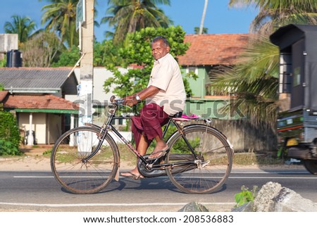 HIKKADUWA, SRI LANKA - FEBRUARY 24, 2014: Elderly man in sarong and shirt riding a bicycle. Cycling is the main transportation for the traditional people in the country.