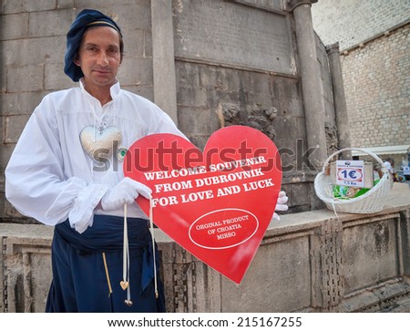 DUBROVNIK, CROATIA - MAY 27, 2014: Man wearing old traditional clothes holding big souvenir heart in front of Onofrio\'s fountain. Dubrovnik has many shops selling authentic local craft and souvenirs.